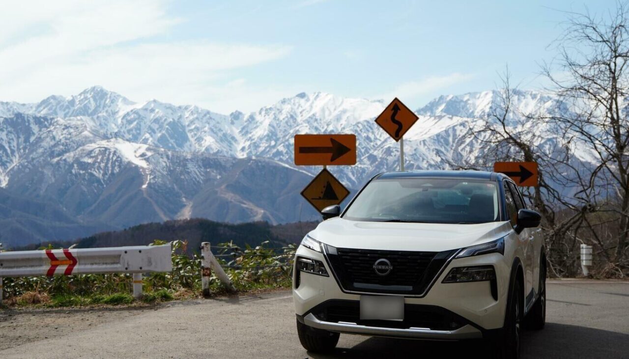 雪山を背景に山道に停車している白い日産 エクストレイル(T33型)。大自然のアウトドアやドライブで活躍するエクストレイル SUVの良さが伝わる風景写真