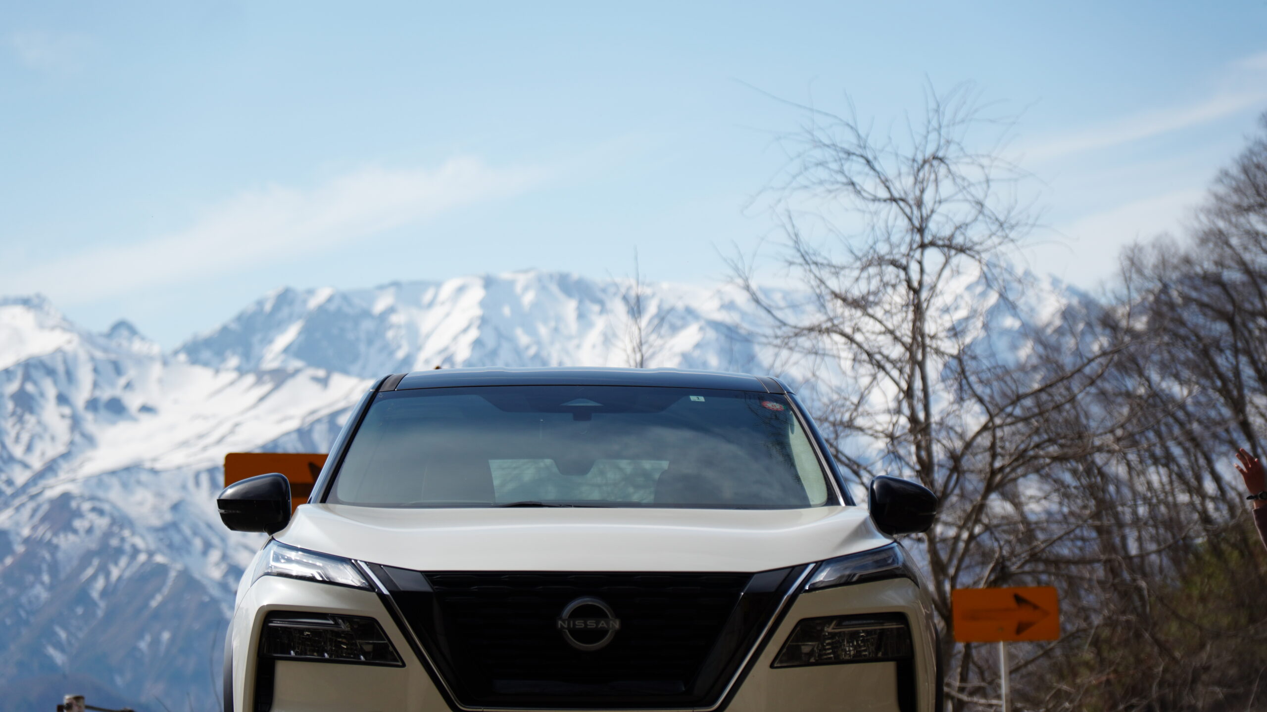 冠雪した山脈を背景に自然の中をドライブする白い日産エクストレイルのフロントビュー